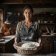 Portrait of head recipe tester Clara Vance holding a linen-lined proofing basket in a dark rustic kitchen